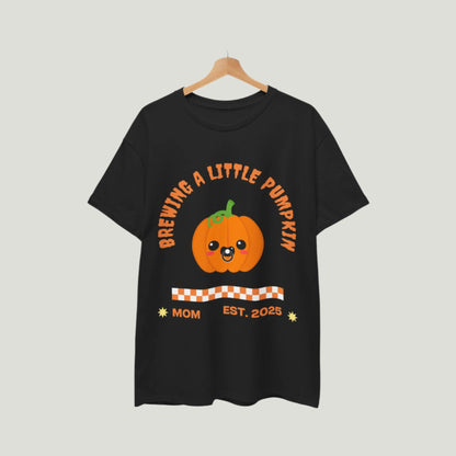  Brewing A Little Pumpkin T-Shirt in black color featuring an adorable pumpkin with a pacifier and the text "Brewing a Little Pumpkin, Mom Established 2025." This charming and comfortable tee is perfect for announcing a pregnancy during Halloween, making it a delightful choice for expecting parents. Ideal for festive celebrations, family gatherings, and capturing memorable photos!