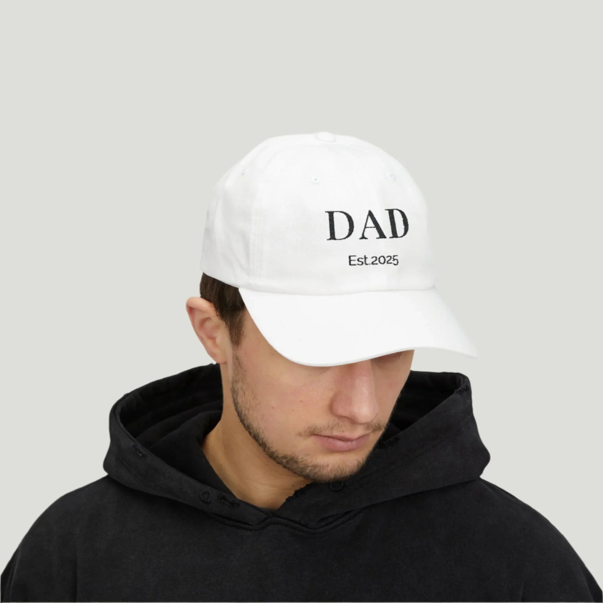 young man wearing Classic Dad Cap in white color with  a stylish design featuring the word "Dad" embroidered in black thread, with "Established 2025" underneath.