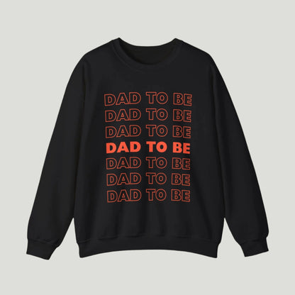 Black color Dad To Be Sweatshirt featuring bold orange lettering with the phrase "Dad To Be" repeated multiple times. Ideal for announcing pregnancy to expectant fathers in a fun and stylish way. Perfect for celebrating this exciting journey!