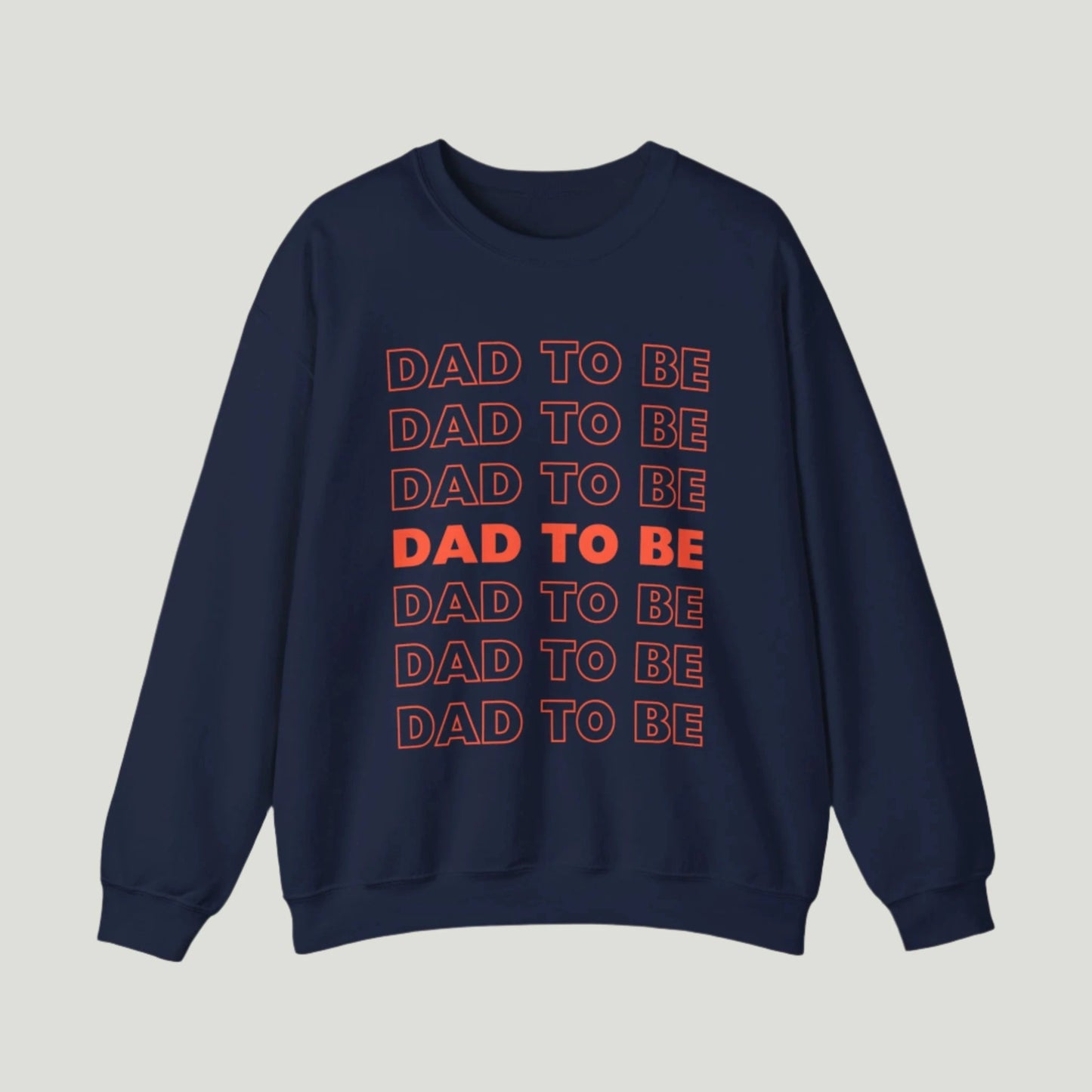 Navy color Dad To Be Sweatshirt featuring bold orange lettering with the phrase "Dad To Be" repeated multiple times. Ideal for announcing pregnancy to expectant fathers in a fun and stylish way. Perfect for celebrating this exciting journey!