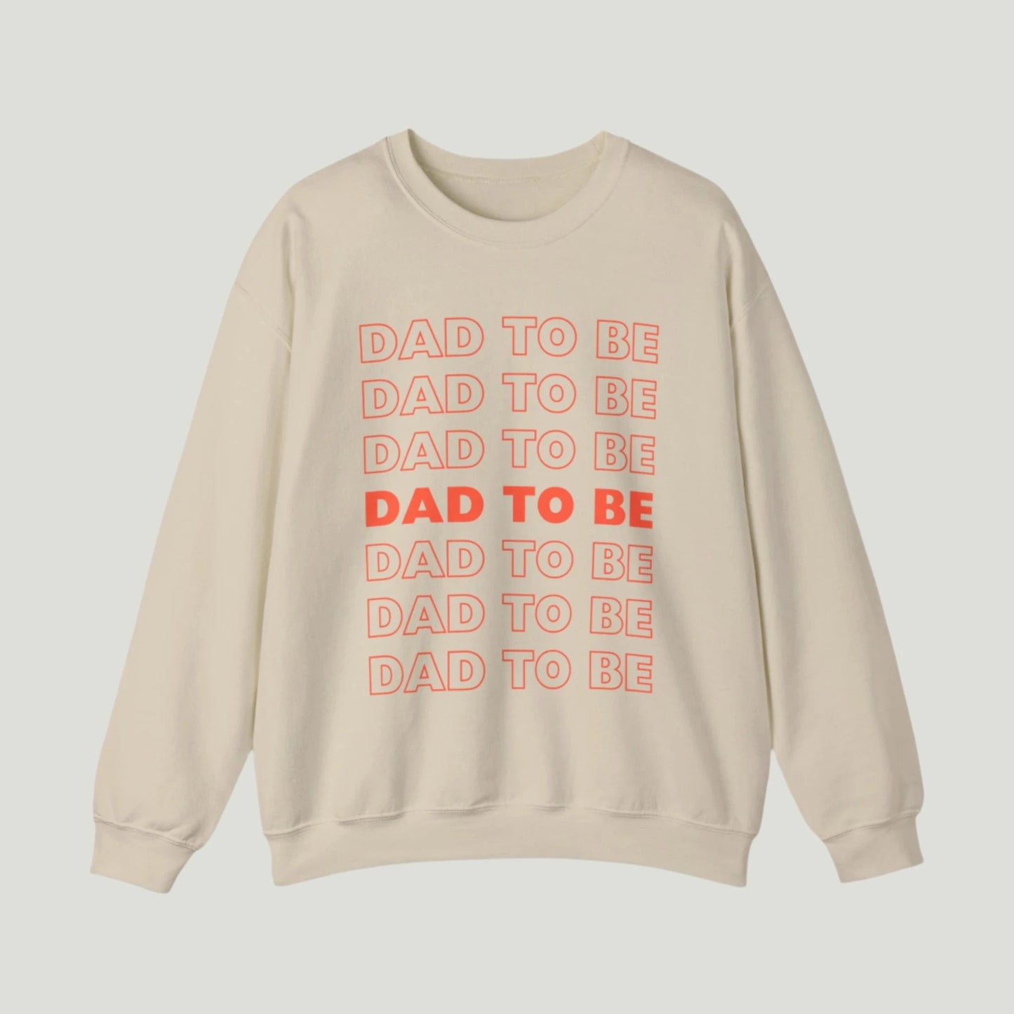 Sand color Dad To Be Sweatshirt featuring bold orange lettering with the phrase "Dad To Be" repeated multiple times. Ideal for announcing pregnancy to expectant fathers in a fun and stylish way. Perfect for celebrating this exciting journey!