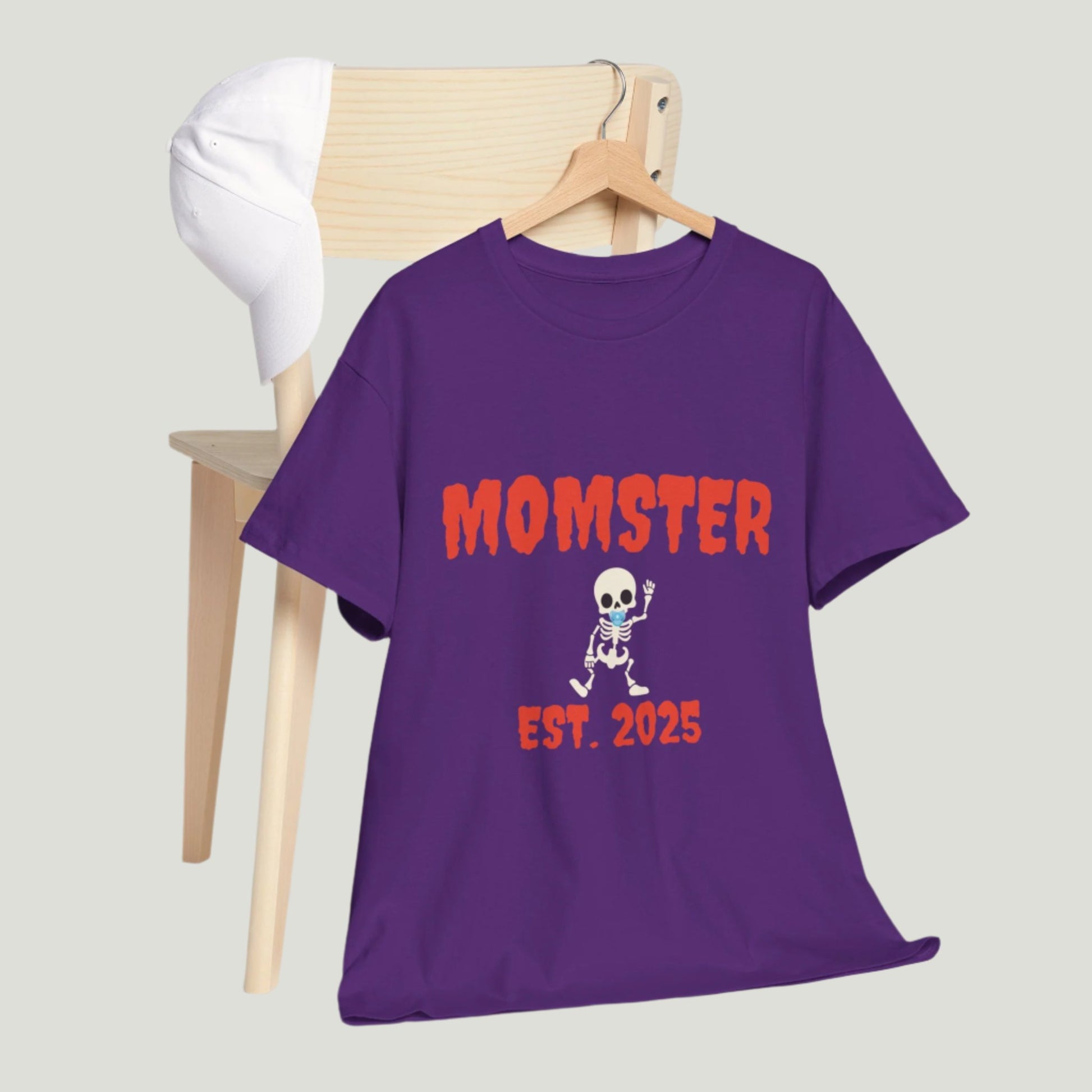 Purple t-shirt featuring red text "Momster Est. 2025," perfect for announcing a pregnancy during Halloween, showcasing a playful and festive design.