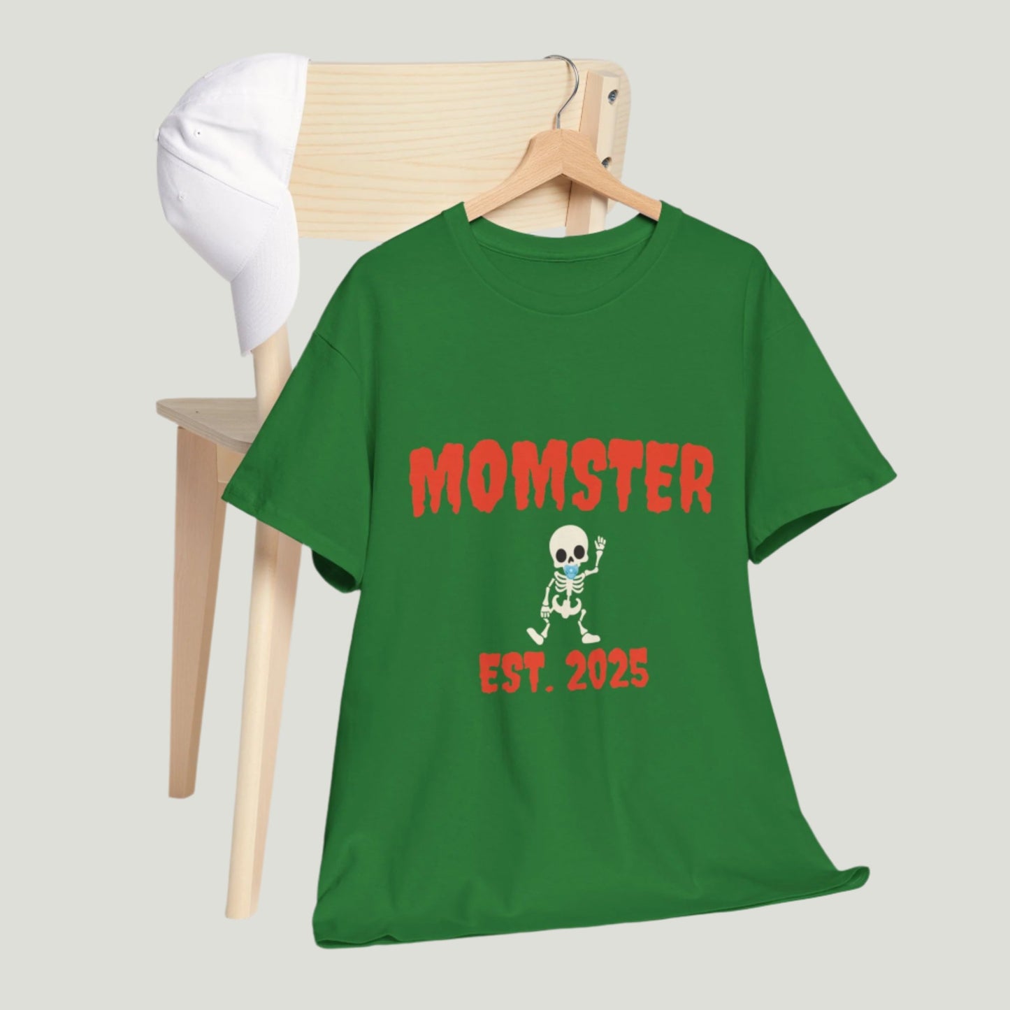 turf Green t-shirt featuring red text "Momster Est. 2025," perfect for announcing a pregnancy during Halloween, showcasing a playful and festive design.