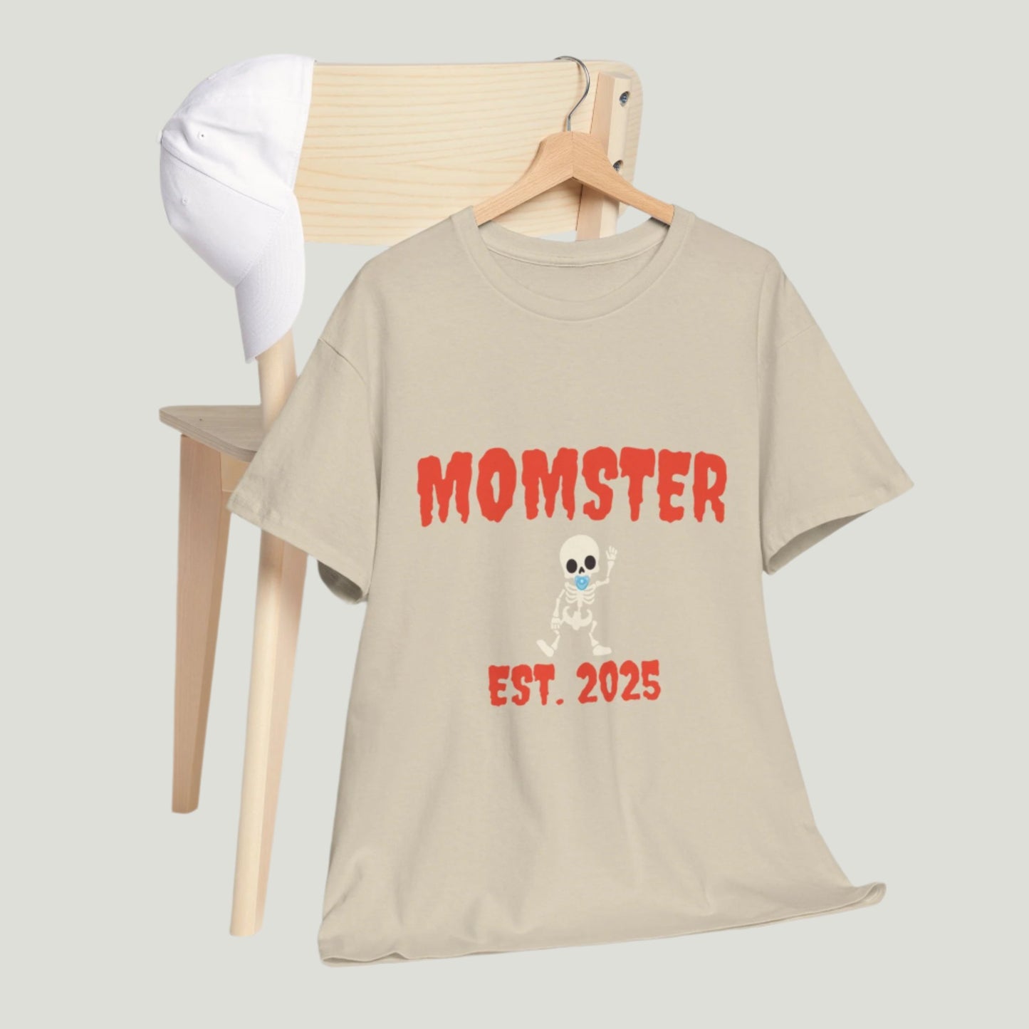 Sand t-shirt featuring red text "Momster Est. 2025," perfect for announcing a pregnancy during Halloween, showcasing a playful and festive design.