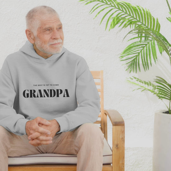 Video of a grandfather seated enjoying his Grey sweatshirt with black text reading "The Best Is Yet To Come GRANDPA," perfect for announcing a pregnancy to soon-to-be grandparents.