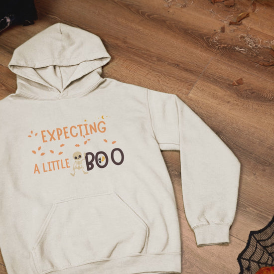 Haunted themed video of an Expecting A Little Boo hoodie placed on a wooden surface with halloween decorations