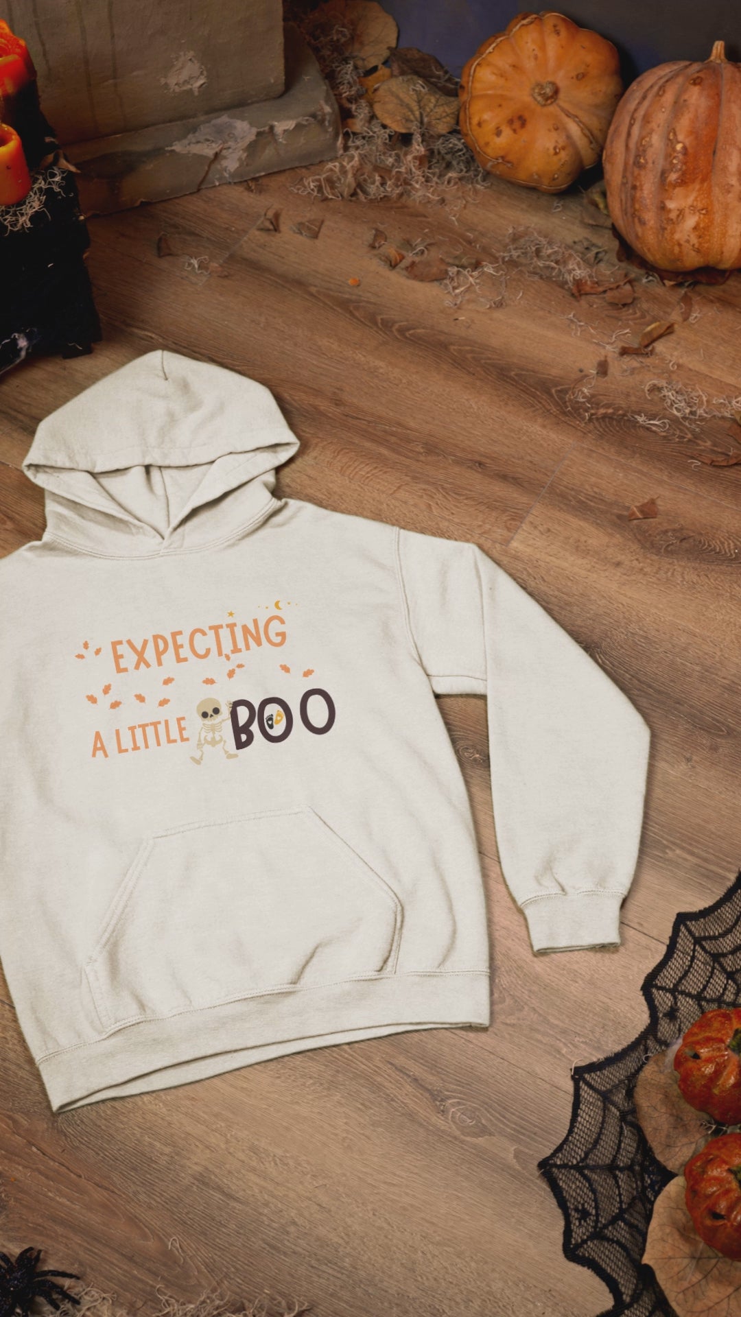 Haunted themed video of an Expecting A Little Boo hoodie placed on a wooden surface with halloween decorations